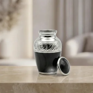 Black Elegance Keepsake Urn resting on a light oak shelf, surrounded by warm ambient light and soft background bokeh