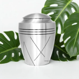 Brushed brass cremation urn next to a monstera plant, in a modern home decor setting.