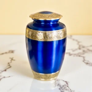 Close-up of ornate gold etched band on a dark blue brass cremation urn lid and body.