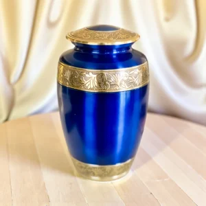 Ornate regal blue and gold brass cremation urn on wood table, traditional funeral ashes memorial.