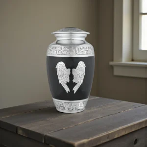 Black and silver 'Midnight Wings' angel urn for adult ashes, displayed in a warm, contemplative home setting on a dark wood table.