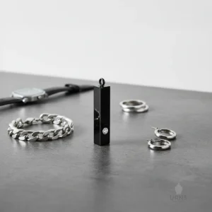 High-angle view of the black Minimalist Bar Urn Necklace with crystal, contrasting against a silver bracelet, rings, and a watch on a dark surface.