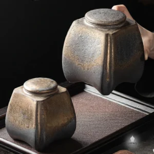A 'Gilded Earth' rustic ceramic pet urn being held, with an identical urn sitting on a traditional dark wood tray, showing its antique bronze finish.