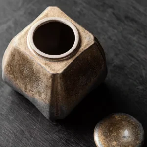 The 'Gilded Earth' ceramic pet urn shown with its lid off, revealing the spacious interior chamber for ashes, resting on a dark wood surface.