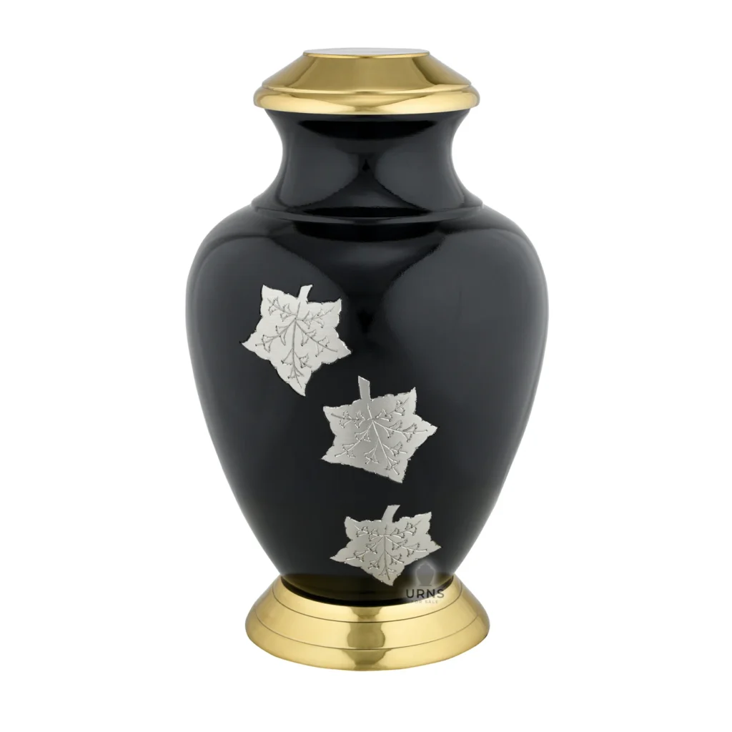 The 'Midnight Maple' solid brass urn in polished black and gold, featuring three silver maple leaf details on the front.