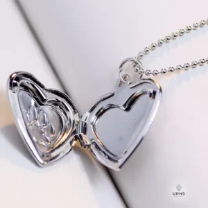 An open silver heart-shaped photo locket, showing the inside frames and the paw print engraving on the front.