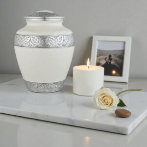 Silver Lining White Adult Cremation Urn in a remembrance setting with a lit candle, single flower, and blurred photo frame.