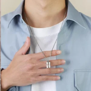 A man wearing the stainless steel urn necklace, holding the clear cylindrical vial pendant in his hand against his chest.
