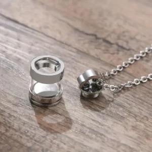 Stainless steel cremation urn necklace for ashes, featuring a clear cylindrical vial pendant on a silver-toned chain against a white background.