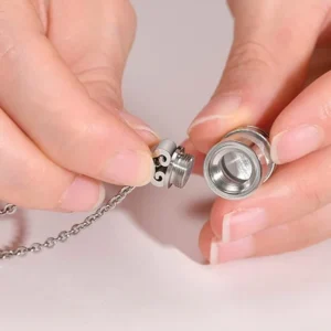 Hands unscrewing the top of a stainless steel urn necklace, showing the secure threaded screw and the hollow inside chamber for holding ashes.