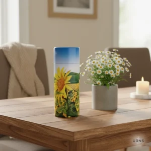 Sunflower Fields Biodegradable Scattering Tube placed on a wooden table beside a vase of white flowers, emphasizing the urn's use as a respectful memorial keepsake in a home interior setting.