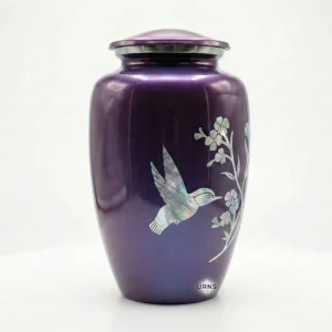 Angled view of the Amethyst Twilight purple cremation urn, highlighting the iridescent hummingbird in mid-flight against the metallic finish.