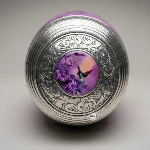 Direct top view of the Sunrise Serenade adult cremation urn, focusing on the intricately engraved silver lid with its central painted purple hummingbird and flower medallion.