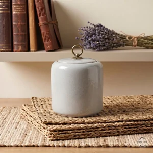 The Alabaster Zen Ceramic Cremation Urn styled on a shelf with antique books and a dried lavender bouquet, showcasing its elegant home decor appeal.