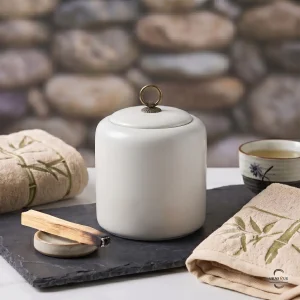 Close-up of the Alabaster Zen Ceramic Cremation Urn on a slate tray with a burning Palo Santo stick and embroidered bamboo towels for a peaceful atmosphere.