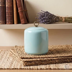 The Celeste Zen Ceramic Cremation Urn styled on a shelf with antique books and a dried lavender bouquet, showcasing its elegant home decor appeal.
