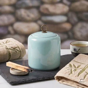 Close-up of the Alabaster Zen Ceramic Cremation Urn on a slate tray with a burning Palo Santo stick and embroidered bamboo towels for a peaceful atmosphere.