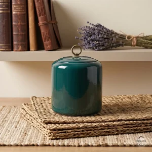 The Emerald Zen Ceramic Cremation Urn styled on a shelf with antique books and a dried lavender bouquet, showcasing its elegant home decor appeal.