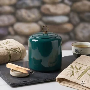 Close-up of the Emerald Zen Ceramic Cremation Urn on a slate tray with a burning Palo Santo stick and embroidered bamboo towels for a peaceful atmosphere.