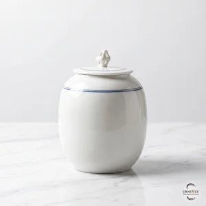 A high-gloss white handcrafted ceramic storage urn featuring a blue fillet line and a traditional red seal, shown on a white marble surface.
