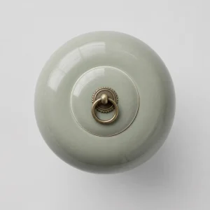 Minimalist light green ceramic cremation urn with high-gloss polished finish and a decorative brass ring handle on the lid.