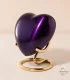 A glossy, deep purple heart-shaped keepsake urn resting securely on an elegant, modern gold wire display stand, set against a soft, neutral background.