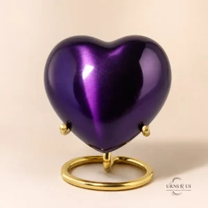 Straight-on front view of a glossy, deep plum purple heart-shaped keepsake urn, balanced symmetrically on a curved gold wire display stand.