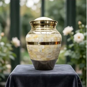 A Pearl Petal Adult Brass Cremation Urn for Ashes displayed outdoors on a table covered with a dark grey cloth, with roses and greenery in the background.