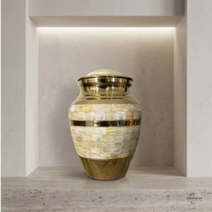 Front view of a Pearl Petal Adult Brass Cremation Urn with a mother-of-pearl inlay and gold accents, displayed on a stone shelf in a modern niche with subtle lighting.