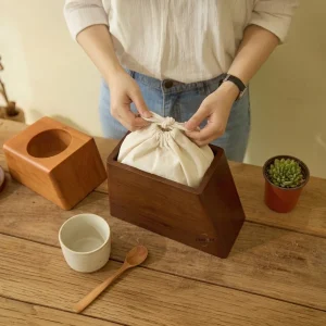 A person carefully placing a cloth ash pouch inside a dark handcrafted wooden cremation urn by Urns R Us on a rustic table.