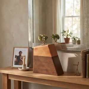 A modern two-tone wooden planter cremation urn holding a small succulent, displayed on a wooden console table next to a framed photo and candle in a home interior.