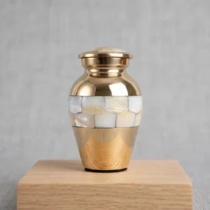 Small brass keepsake cremation urn featuring a white mother-of-pearl inlay band, resting on a wooden display stand.