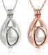 A close-up view of two teardrop-shaped cage locket pendants, one in polished silver and one in rose gold, each hanging from a matching chain on a white background. Inside each open cage is a segmented silver sound ball.