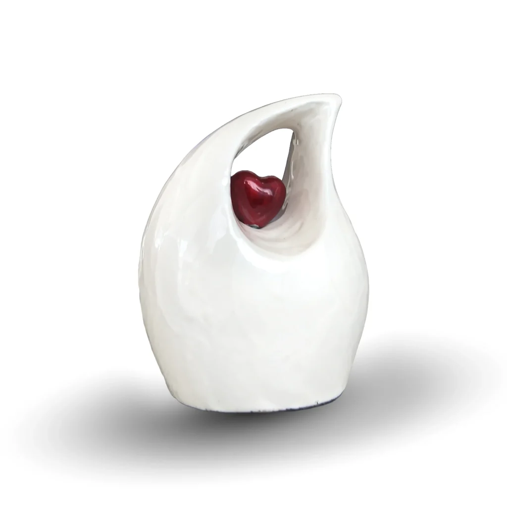 White teardrop keepsake urn for ashes featuring a suspended small red heart, isolated on a white background.