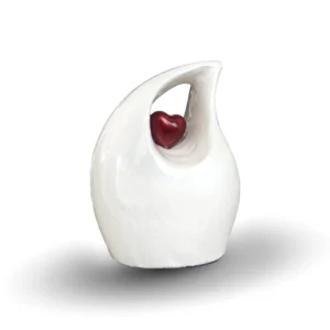 White teardrop keepsake urn for ashes featuring a suspended small red heart, isolated on a white background.